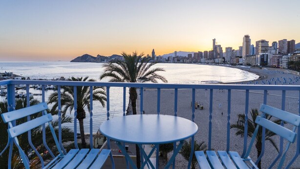 A balcony with a table and chairs overlooking a beach and cityscape during sunset. - Luxury penthouse with sea views (Benidorm)