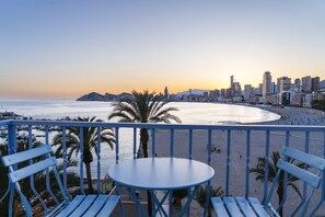 A balcony with a table and chairs overlooking a beach and cityscape during sunset. - Luxury penthouse with sea views (Benidorm)