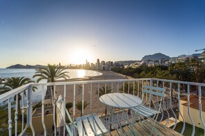 A balcony with a table and chairs overlooking a beach with a city skyline in the background.