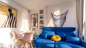 A modern living room with a blue sofa, a hanging chair, and a dining area with chairs and a table. - Luxury penthouse with sea views (Benidorm)