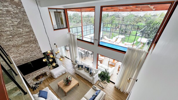 Een ruime woonkamer met een groot raam dat uitkijkt over een zwembad en tuin, een open haard en een eethoek.
