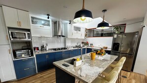 Een moderne keuken met blauwe kasten, een roestvrijstalen koelkast, een magnetron, een fornuis en een bargedeelte met barkrukken.