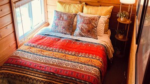 A cozy wooden cabin bedroom with a bed, colorful bedding, a window, and a painting on the wall. - >>The Daydream Lodge<<
@Racers Ridge (Plymouth)