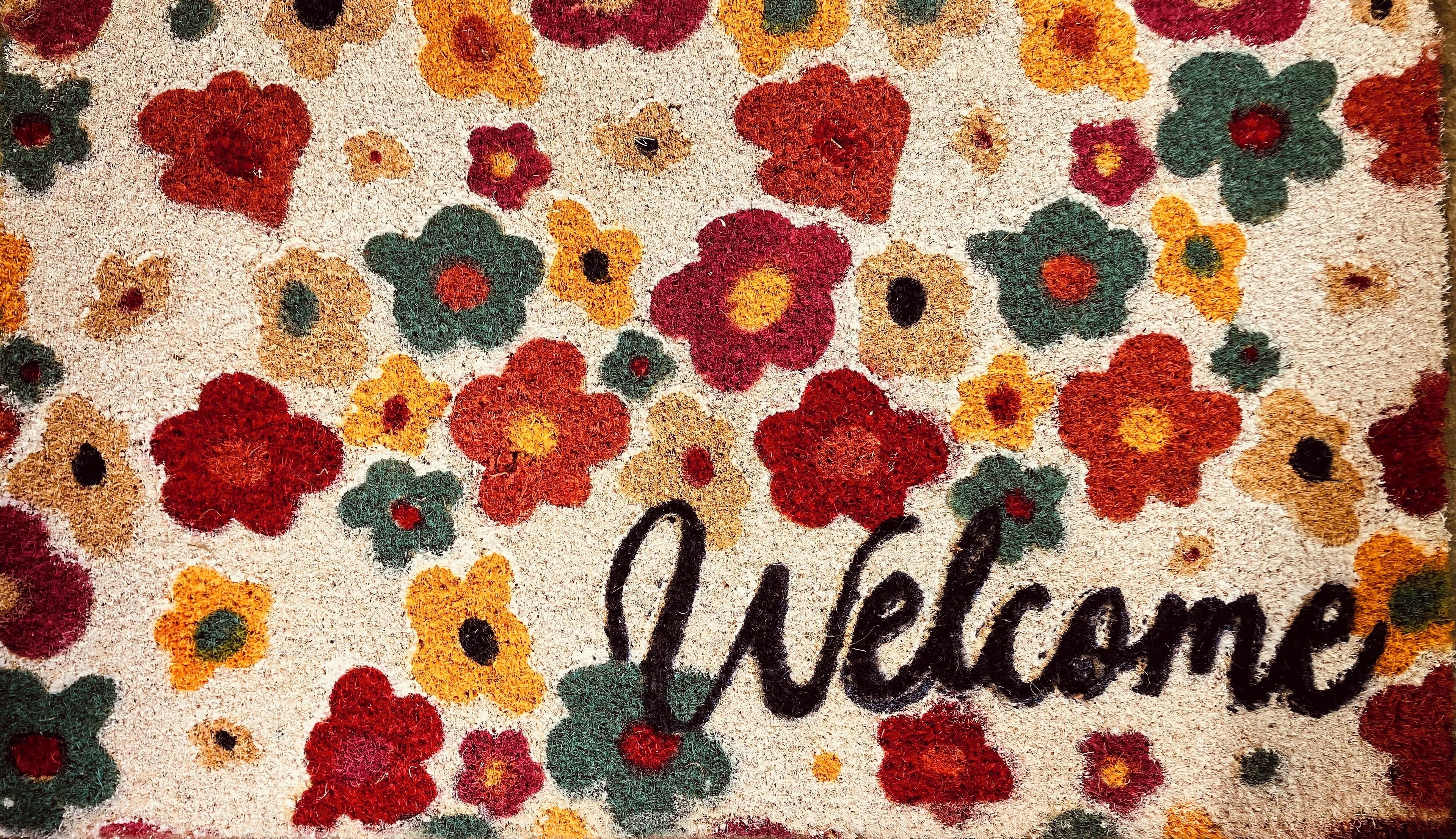 A colorful welcome mat with a floral pattern and the word "Welcome" written on it.