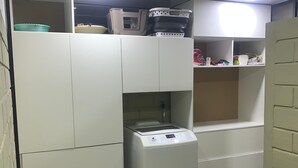 Une cuisine compacte avec des meubles blancs, un lave-linge encastré et un panier à linge bleu.