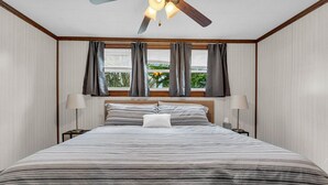 A bedroom with a large bed, two bedside tables, a ceiling fan, and a window with curtains.