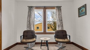 A corner room with two chairs and a small table, a window with curtains, and a framed picture on the wall.