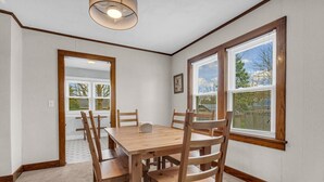 A dining room with a wooden table and chairs, large windows with blinds, and a ceiling light fixture.