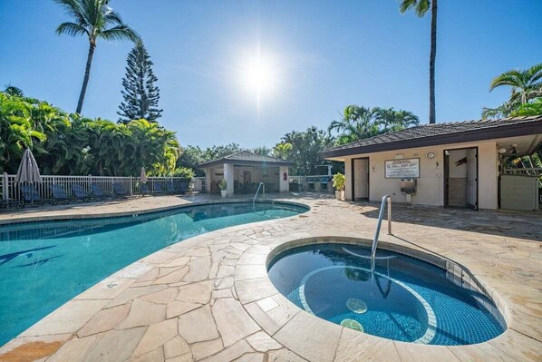 A swimming pool with a stone deck, surrounded by palm trees and a building with a sign.