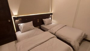 Habitación de hotel con dos camas individuales, cabecero de madera y una puerta.
