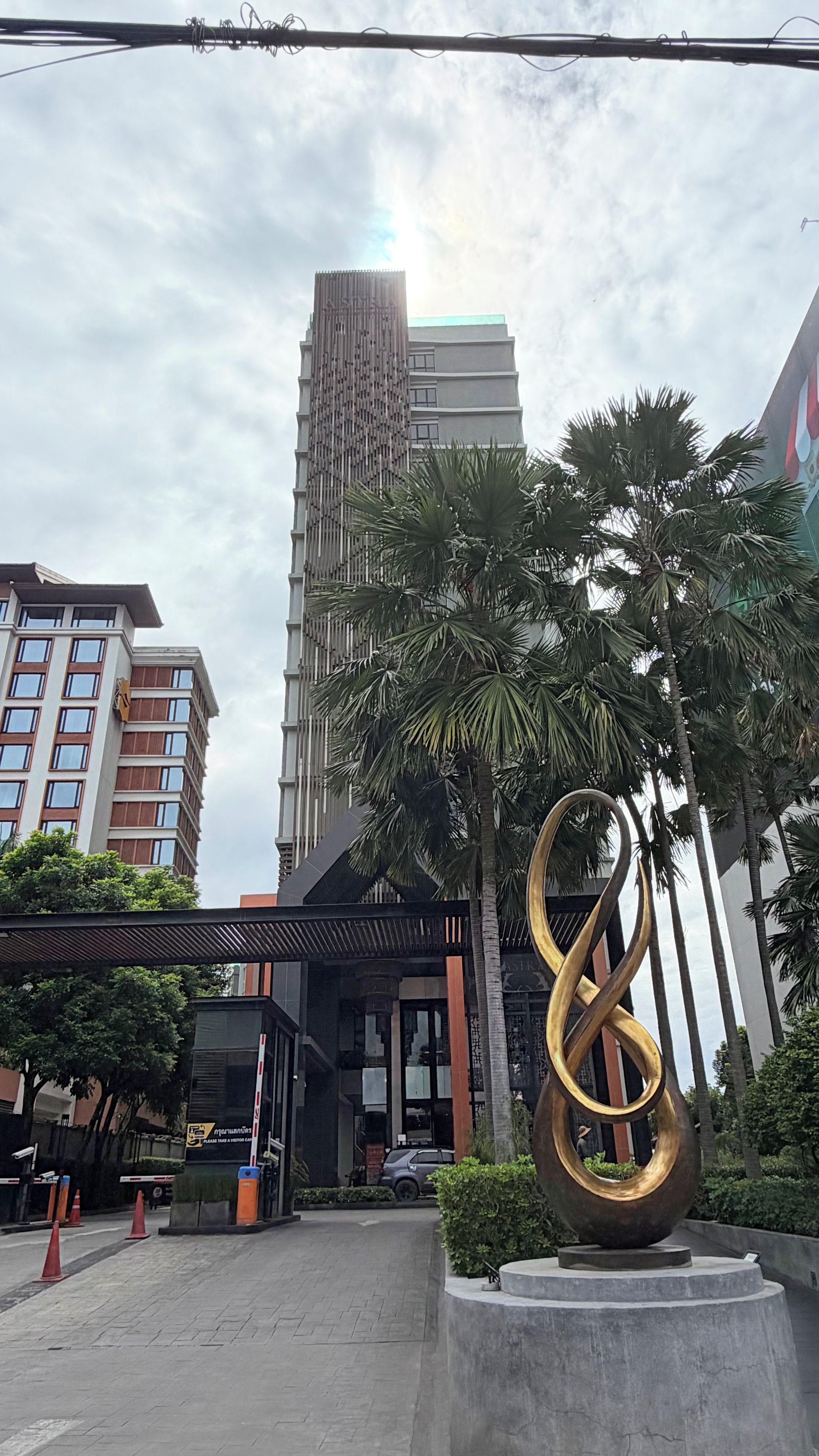 A modern building with a tall structure and a large golden sculpture in the foreground.