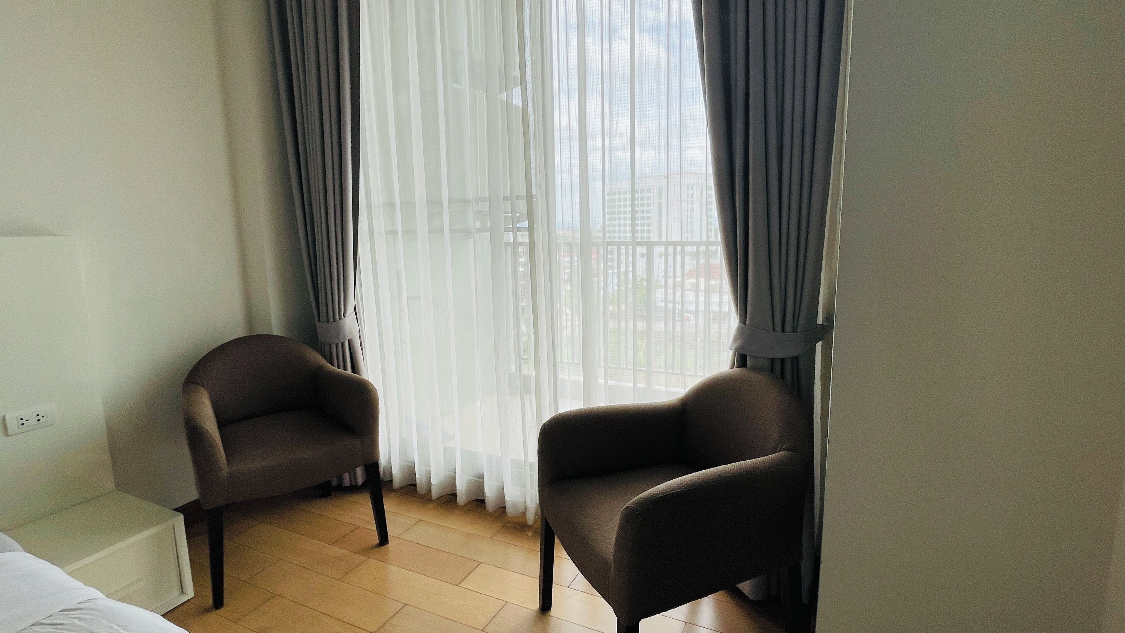 A hotel room with two armchairs, a bed, and a window with sheer curtains.