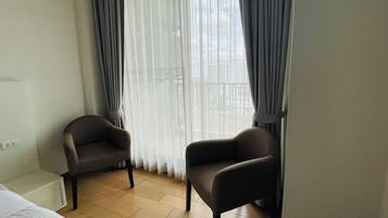 A hotel room with two armchairs, a bed, and a window with sheer curtains.