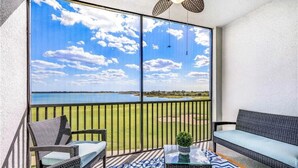 Ein Balkon mit Korbmöbeln, einem gemusterten Teppich und Blick auf einen See und einen Golfplatz.