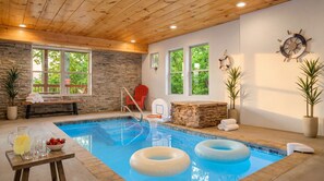 A pool area with stone walls, a wooden ceiling, and a bench with towels.
