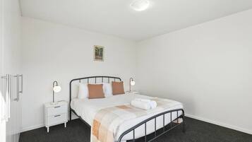Ein Einzelbett mit Metallgestell, ein Nachttisch mit Lampe und ein kleines Bild an der Wand.