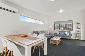 A modern living room with a dining table, two sofas, a coffee table, and a bookshelf.