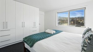 A bedroom with a bed, a window with a view, and a wardrobe. - Spacious Modern Home (Geilston Bay)