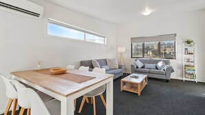 A modern living room with a dining area, grey sofas, a coffee table, and a bookshelf. - Spacious Modern Home (Geilston Bay)