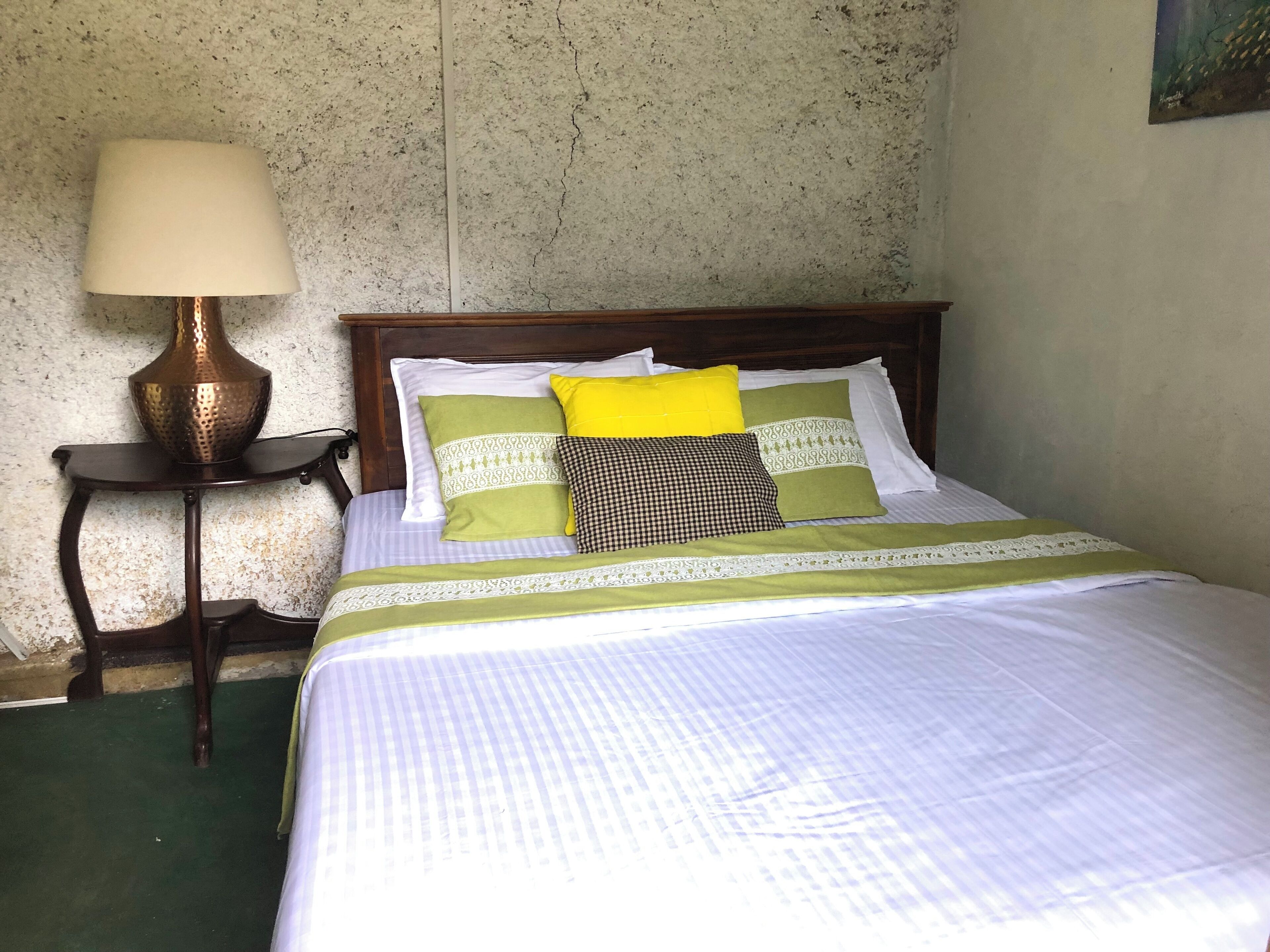 A neatly made bed with a wooden headboard, a bedside table with a lamp, and a textured wall.