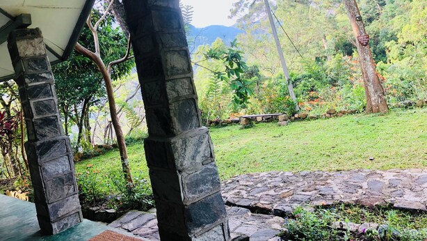 Une structure composée de piliers en pierre, située sous une zone abritée, d’où l’on peut admirer un jardin luxuriant et des montagnes lointaines.