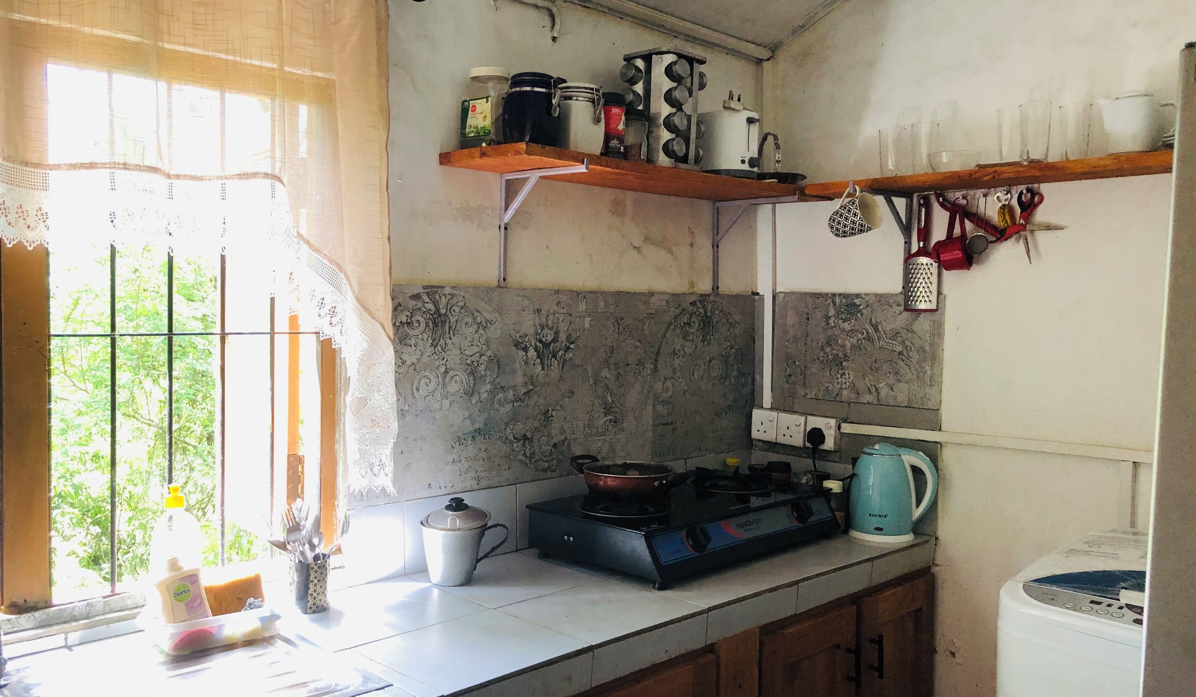 A kitchen with a gas stove, a kettle, and various kitchen utensils on shelves.