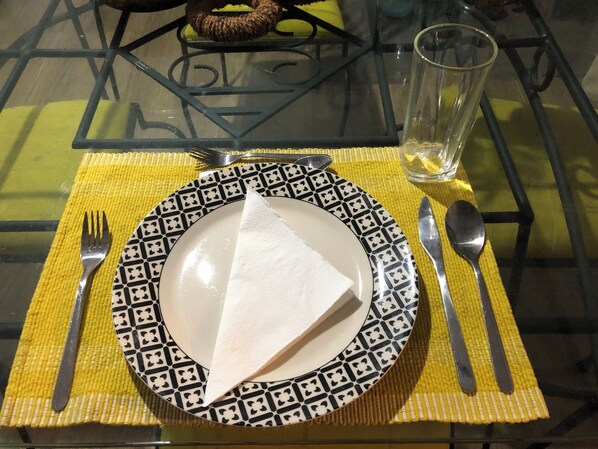 A table set with a patterned plate, a folded napkin, cutlery, and a glass of water on a yellow placemat.