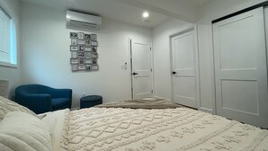 Een slaapkamer met een bed, een blauwe stoel, een wandairconditioner en een deur.