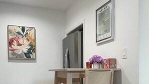 Een kleine keuken met een houten tafel en stoel, een roestvrijstalen koelkast en een afvalbak.