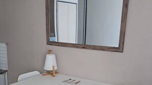 Pieni ruokailutila, jossa on valkoinen pöytä, kaksi tuolia, lamppu ja peili seinällä.