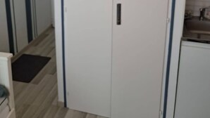 Huone, jossa on valkoinen vaatekaappi, pieni keittokomero ja puulattia.
