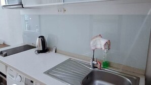 A compact kitchen with a washing machine, a sink with a soap dispenser, and a kettle.
