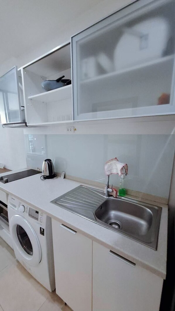 A compact kitchen with a washing machine, a sink with a soap dispenser, and a kettle.