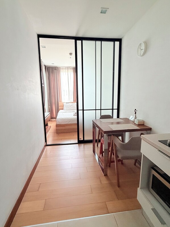 A room with a bed, a dining table with chairs, a kitchen area, and a sliding door leading to another room.