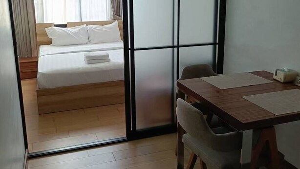 Una habitación de hotel moderna con una cama de madera, una mesa de comedor con sillas y un ventanal corredero que da a un balcón.