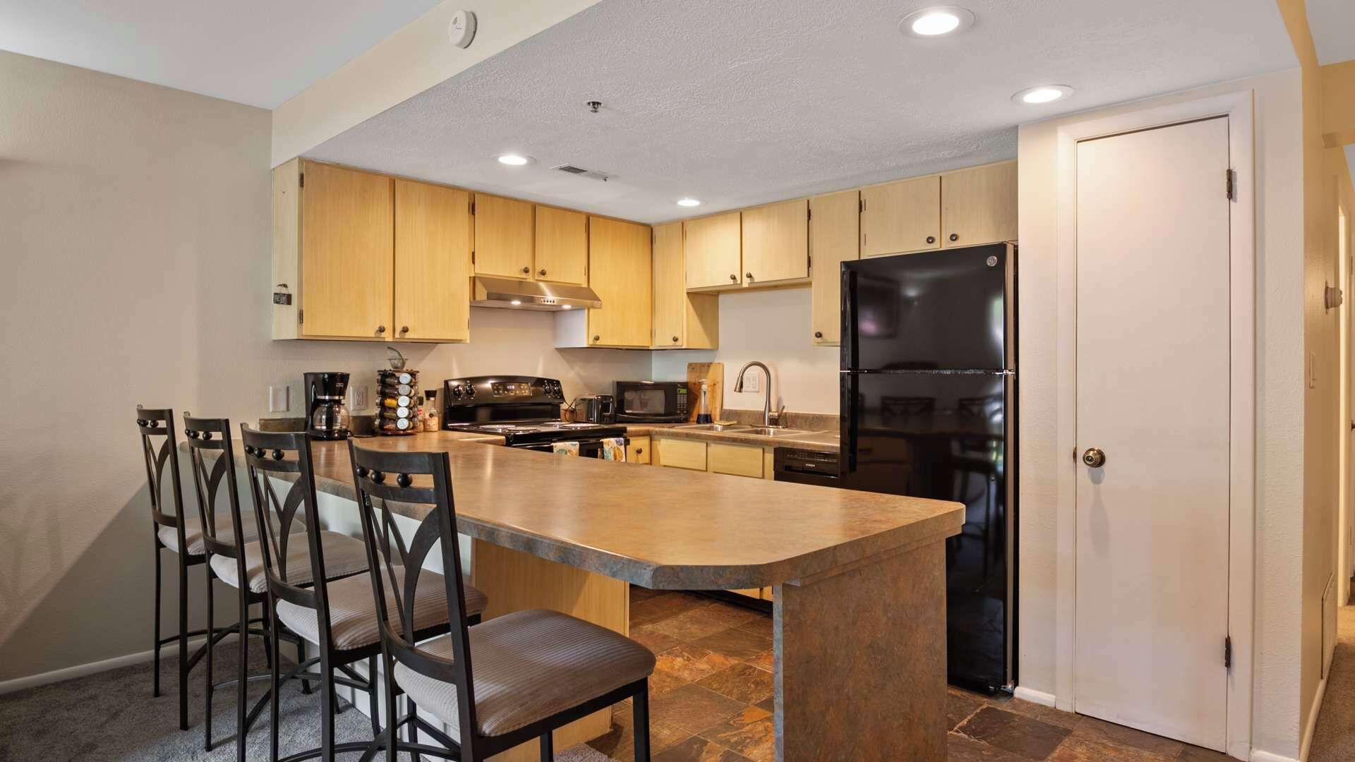 Une cuisine moderne avec des meubles en bois, un réfrigérateur noir, une cuisinière et un grand îlot central doté de tabourets de bar.