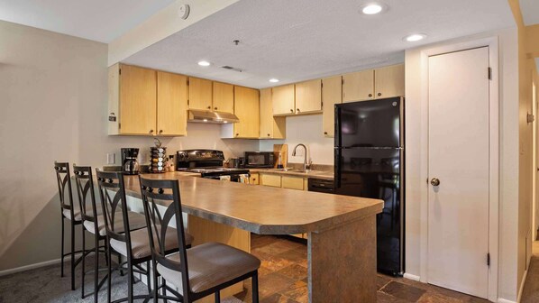 Une cuisine moderne avec des meubles en bois, un réfrigérateur noir, une cuisinière et un grand îlot central doté de tabourets de bar.