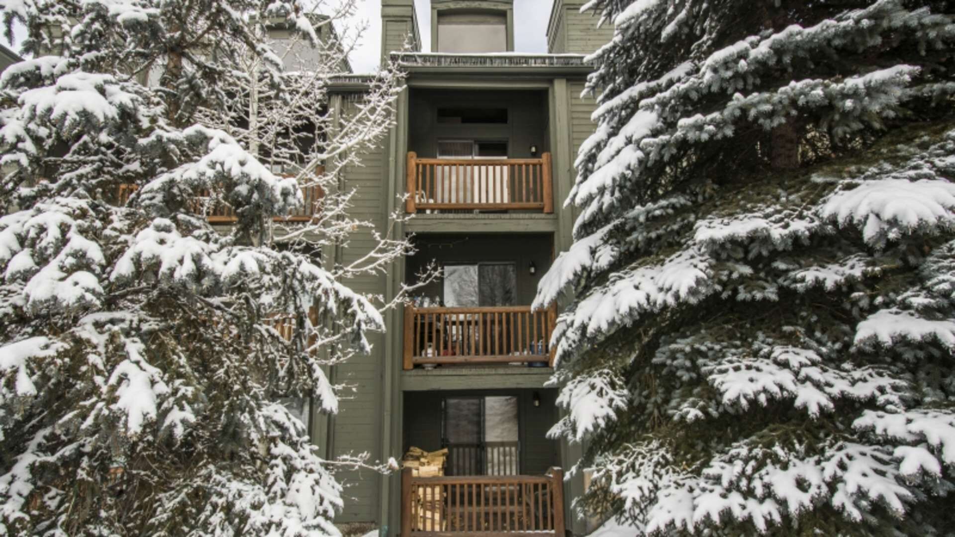 A multi-story building with balconies, surrounded by snow-covered trees.
