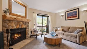 Un salon avec une cheminée en pierre, un canapé, une table basse et un balcon avec vue.