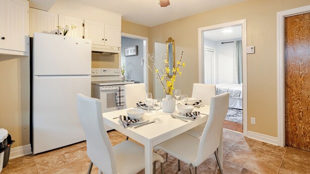 Une cuisine moderne avec des armoires blanches, un four encastré et un coin repas avec une table blanche dressée pour quatre personnes.