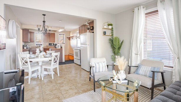 Uma sala de estar moderna com uma mesa de centro de vidro, um sofá cinzento e uma área de refeições com cadeiras brancas.
