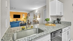 Una cocina moderna con encimeras de granito, electrodomésticos de acero inoxidable y armarios blancos.