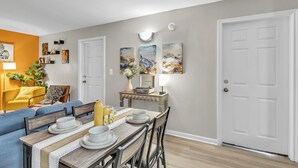 Comedor con una mesa de madera dispuesta para cuatro, flanqueada por dos puertas y una pared decorada con obras de arte.