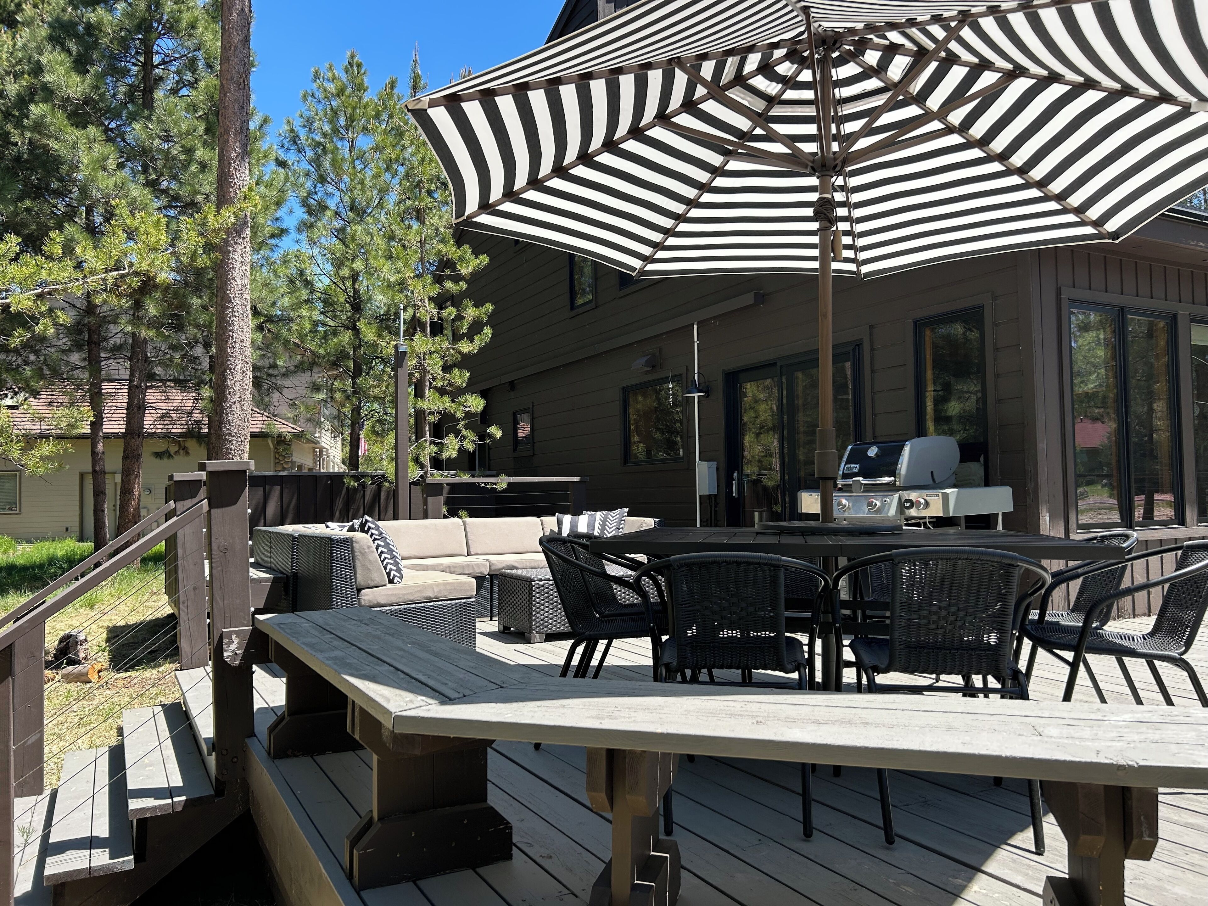 En udendørs terrasse med spisebord, stole og en stor stribet parasol.
