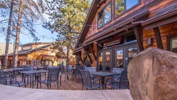 An outdoor patio with tables and chairs, a wooden building with a sign reading "Survived Brewing," and a large rock in the foreground.