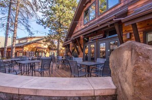Un patio al aire libre con mesas y sillas, un edificio de madera con un letrero que dice 'Survived Brewing' y una roca grande al frente.