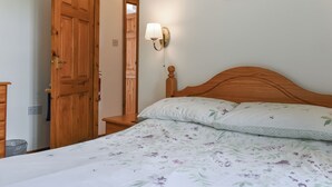 A bedroom with a wooden bed, a nightstand, a wall-mounted lamp, and a door leading to another room.