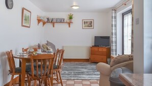 A dining area with a wooden table and chairs, a radiator, a TV on a wooden stand, and a sofa.
