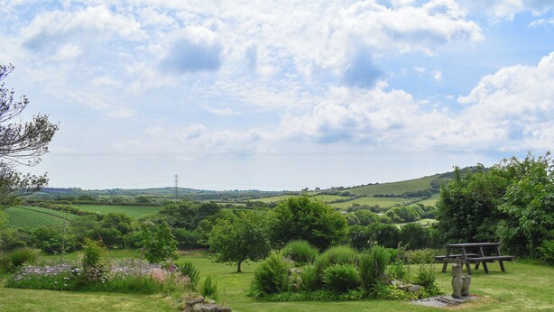 A rural landscape with rolling hills, a picnic table, and a stone sculpture.