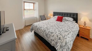Ein Schlafzimmer mit einem großen Bett, einem Nachttisch mit Lampe, einem Fenster mit Jalousien und einer Heizung.